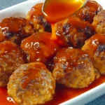 Close-up of golden chicken meatballs on a plate being drizzled with a sticky sweet glaze sauce using a spoon