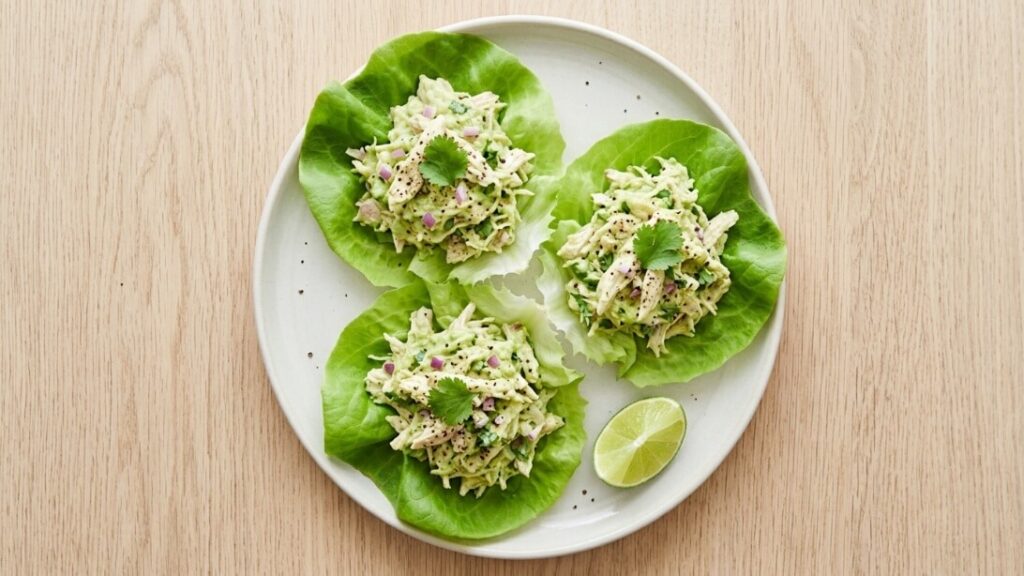 Creamy avocado chicken salad served inside crisp green butter lettuce wraps on a white plate.